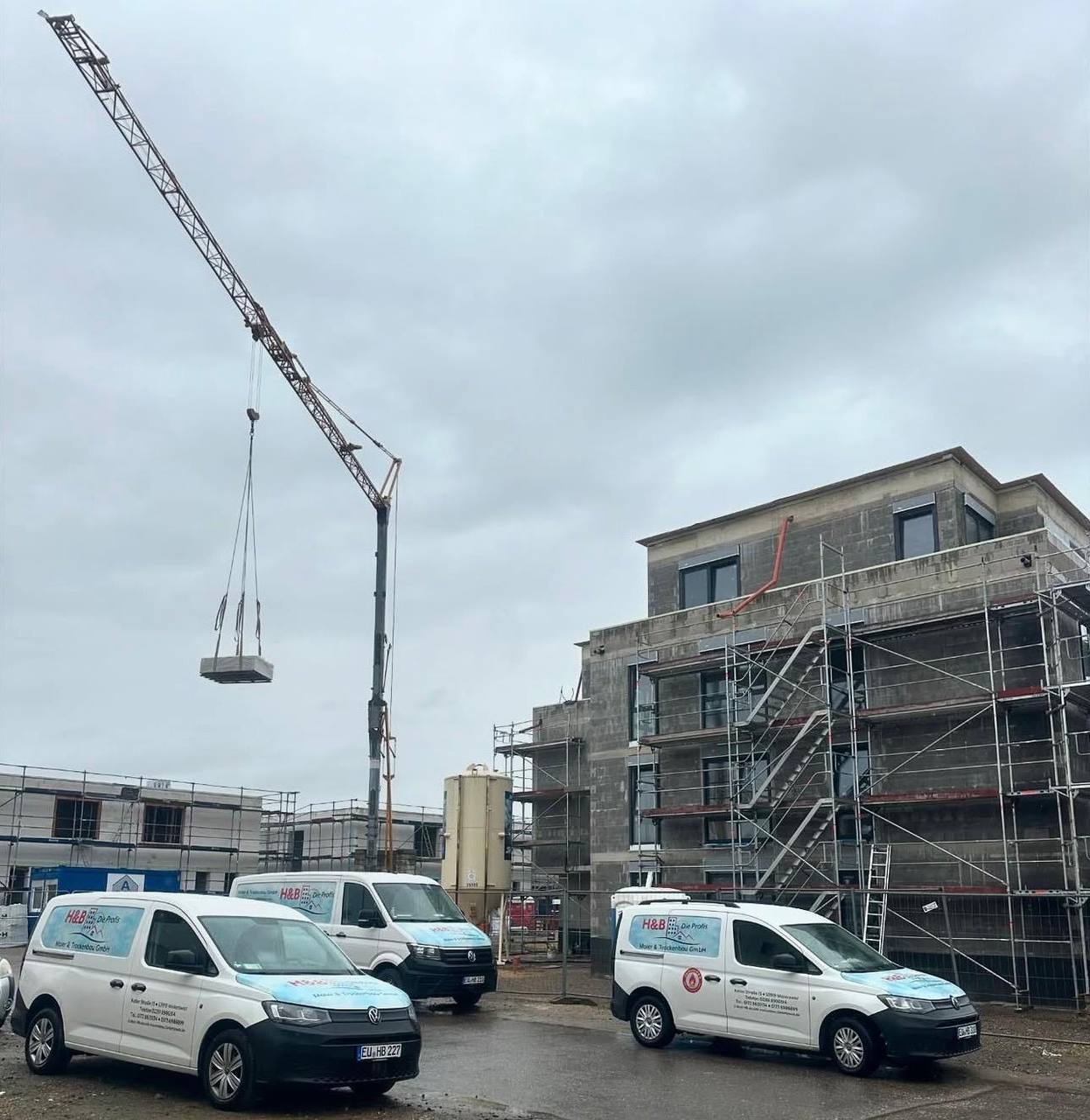 Drei Transporter von H&B Die Profis vor einem Neubau mit Gerüst und Kran