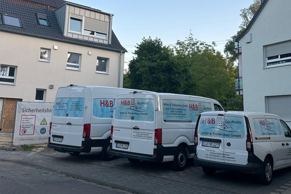 Drei Transporter von H&B Die Profis vor einem Wohnhaus mit Baustelle