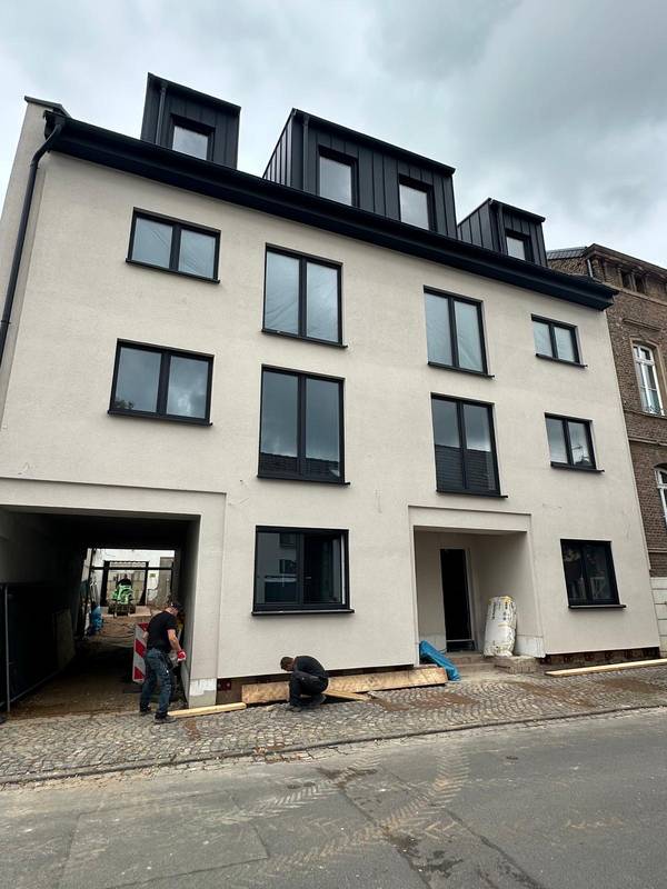 Helle Putzfassade eines Mehrfamilienhauses mit dunklen Fenstern